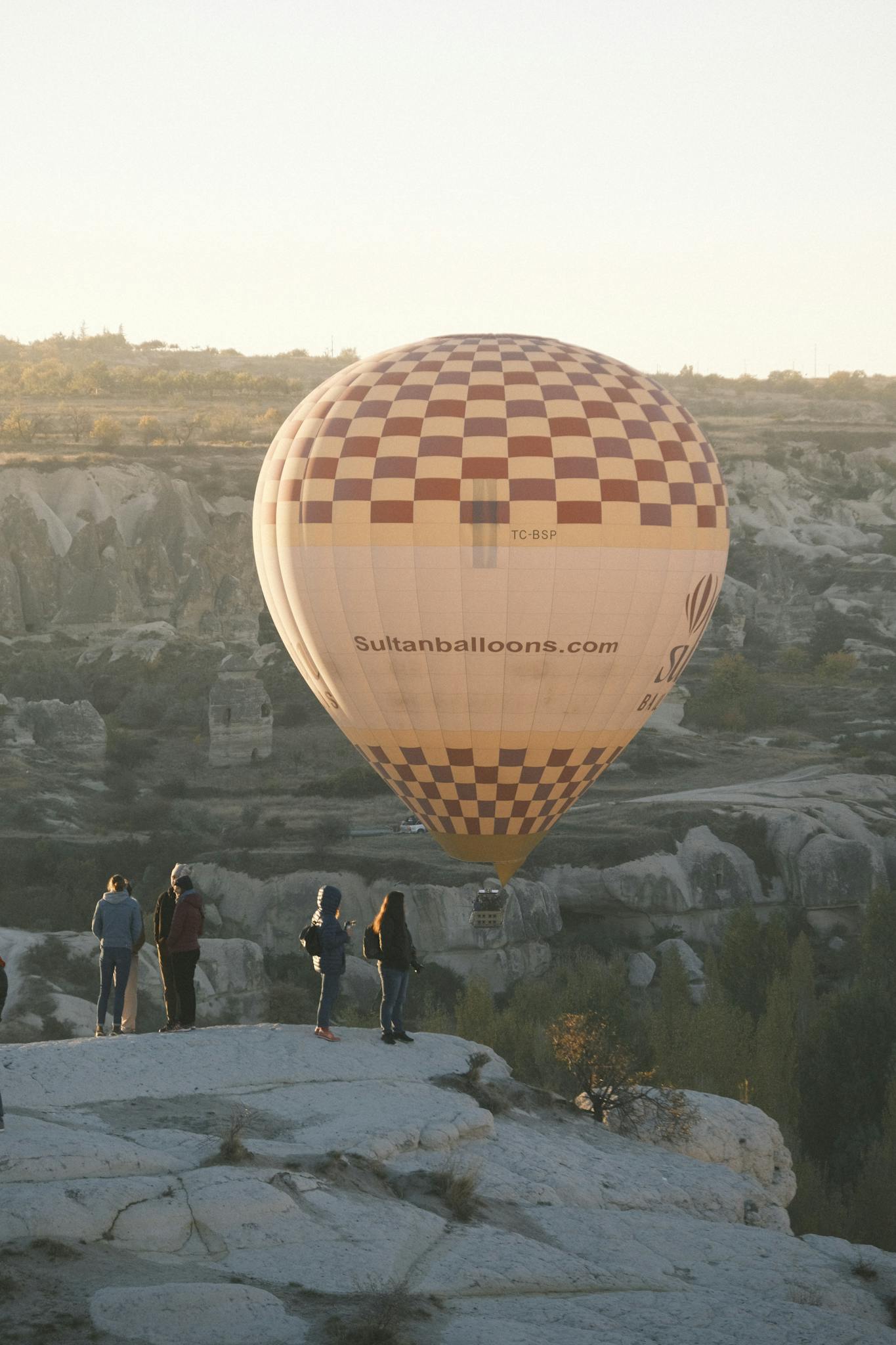 People watching a hot air balloon floating above the unique rocky formations in Cappadocia, Turkey.