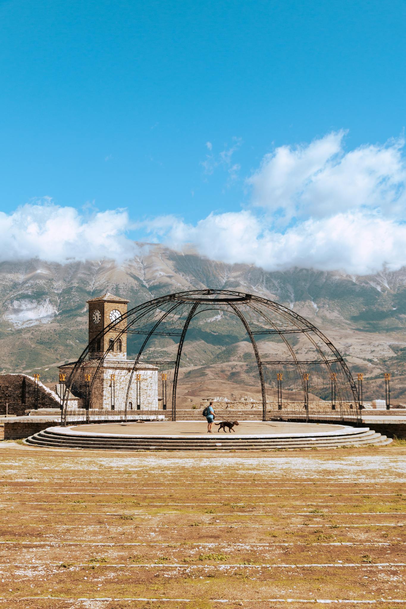 Person walking a dog by Gjirokaster Fortress with mountains in the background, capturing Albania's scenic beauty.